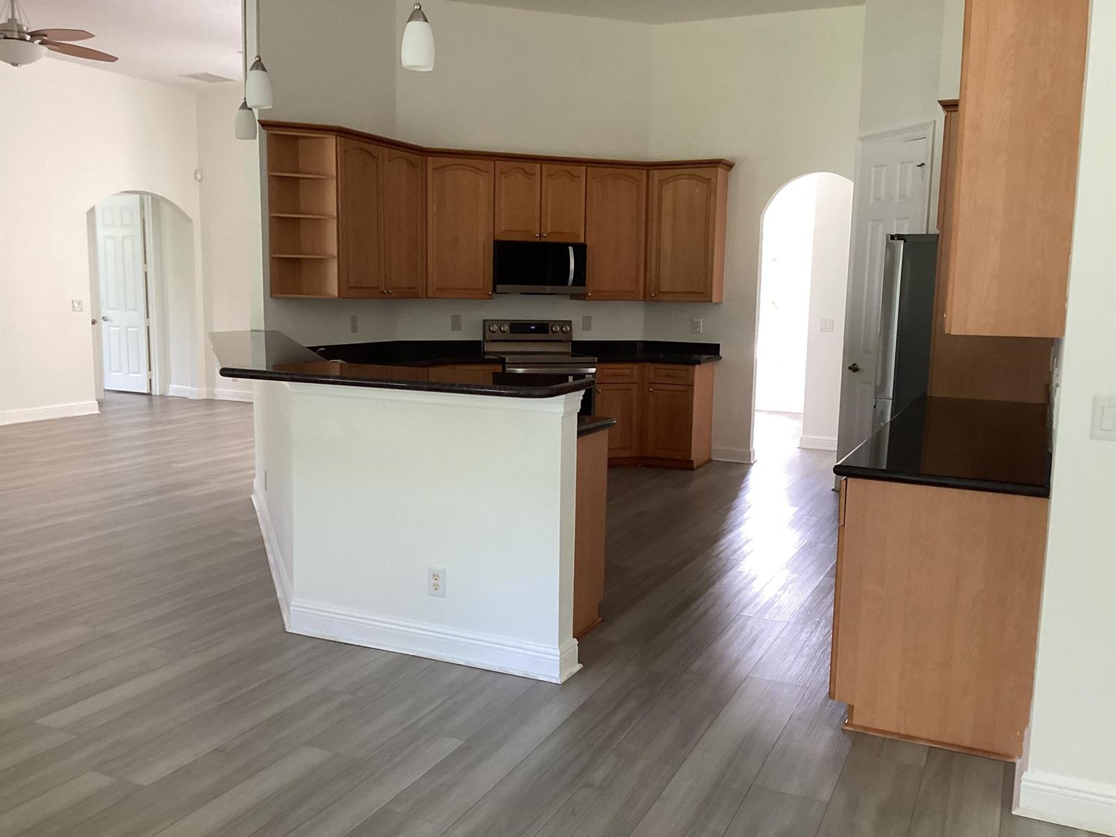 A kitchen with wood cabinets, black countertops, and light gray wood-look flooring — 17119 Alexander Run, Jupiter FL 33478, JUPITER, FL
