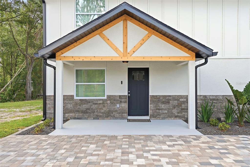 A covered front porch with a wood-truss gable, stone veneer, and a dark entry door — 31848 HEDGEROW DRIVE, WESLEY CHAPEL, FL