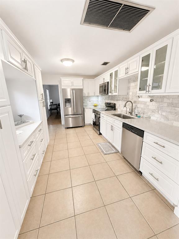 A kitchen features white cabinets, stainless steel appliances, a tile backsplash, and light-colored floor tiles — 2210 NEEDLE PALM DRIVE, EDGEWATER, FL
