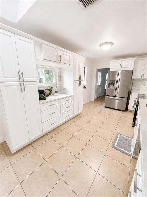 A bright kitchen features white cabinetry, stainless steel appliances, and light-colored tile flooring — 2210 NEEDLE PALM DRIVE, EDGEWATER, FL