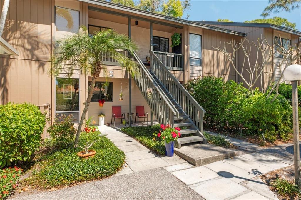 A two-story apartment building exterior features a wooden staircase leading to an upper balcony — 1708 GLENHOUSE DRIVE UNIT 313, SARASOTA, FL