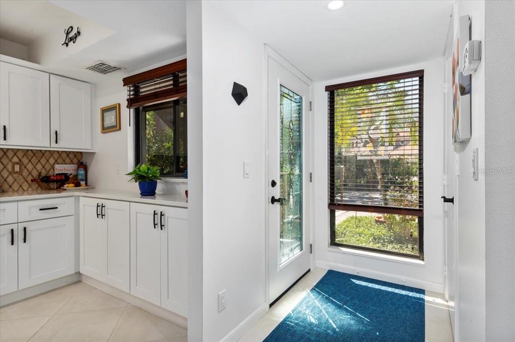 A kitchen area with white cabinets and a tile backsplash sits beside an entryway door — 1708 GLENHOUSE DRIVE UNIT 313, SARASOTA, FL