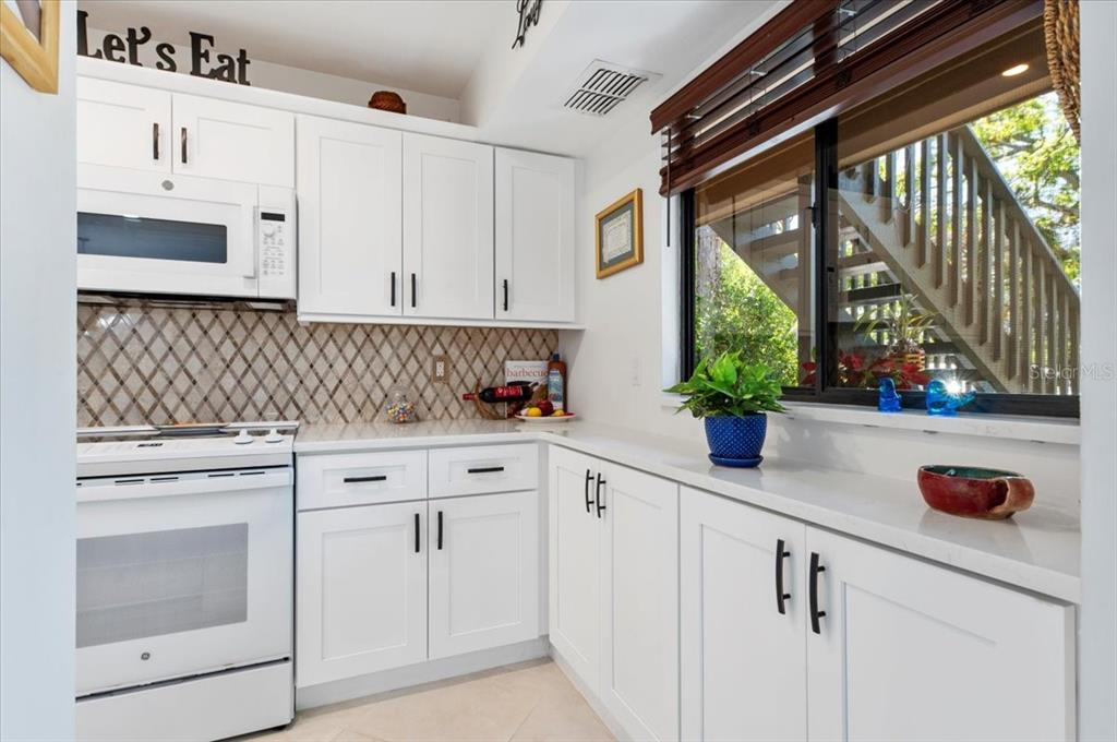 A white kitchen features white cabinets, a microwave, a stove, and a window with blinds — 1708 GLENHOUSE DRIVE UNIT 313, SARASOTA, FL