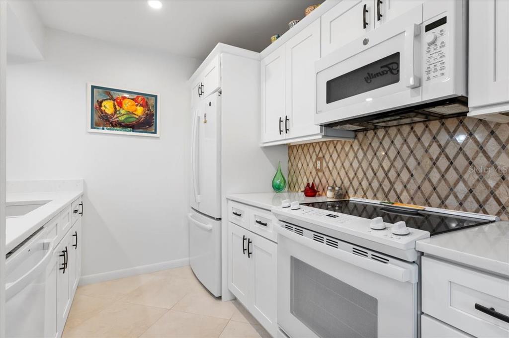 A white kitchen features white cabinetry, a glass-top stove, and a diamond-patterned tile backsplash — 1708 GLENHOUSE DRIVE UNIT 313, SARASOTA, FL