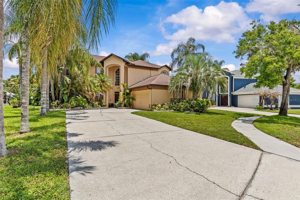A two-story tan house with a concrete driveway and palm trees in the front yard — 27221 SEA BREEZE WAY, WESLEY CHAPEL, FL