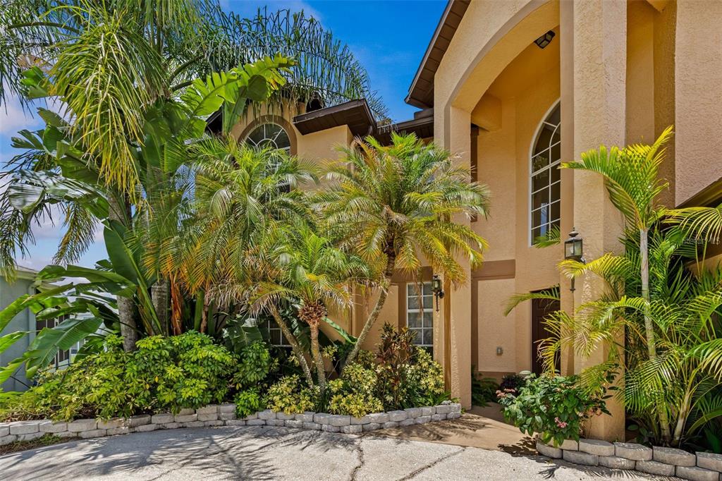 A two-story stucco house exterior features a curved driveway, arched windows, and lush tropical landscaping — 27221 SEA BREEZE WAY, WESLEY CHAPEL, FL