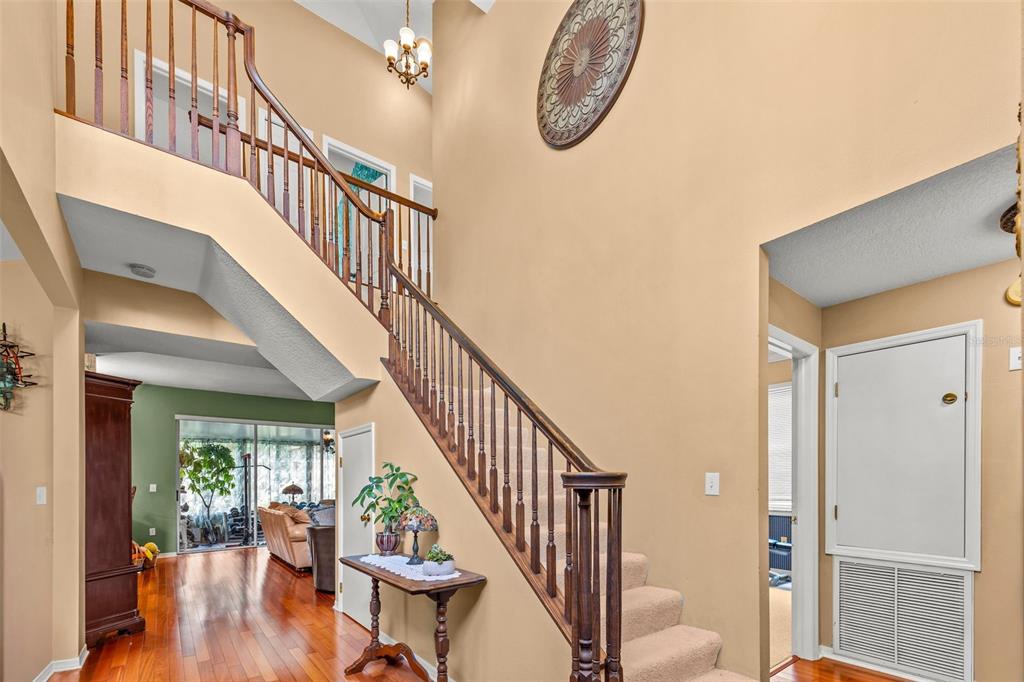 A foyer features a wooden staircase with carpeted steps, hardwood flooring, and a high ceiling — 27221 SEA BREEZE WAY, WESLEY CHAPEL, FL