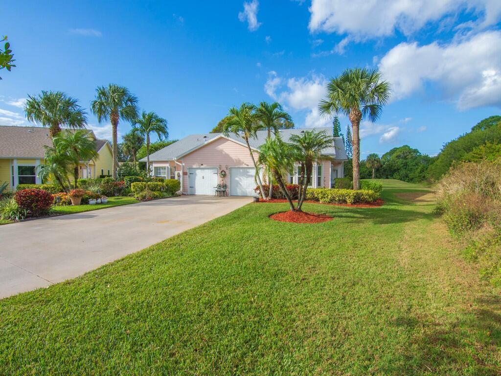 A light pink house with a two-car garage and palm trees sits on a lawn — 4001 Gator Trace Road, Fort Pierce FL 34982, FORT PIERCE, FL