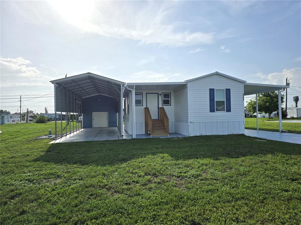 A white manufactured home features a metal carport, a covered porch, and wooden stairs — 1359 IBIS DRIVE, ENGLEWOOD, FL