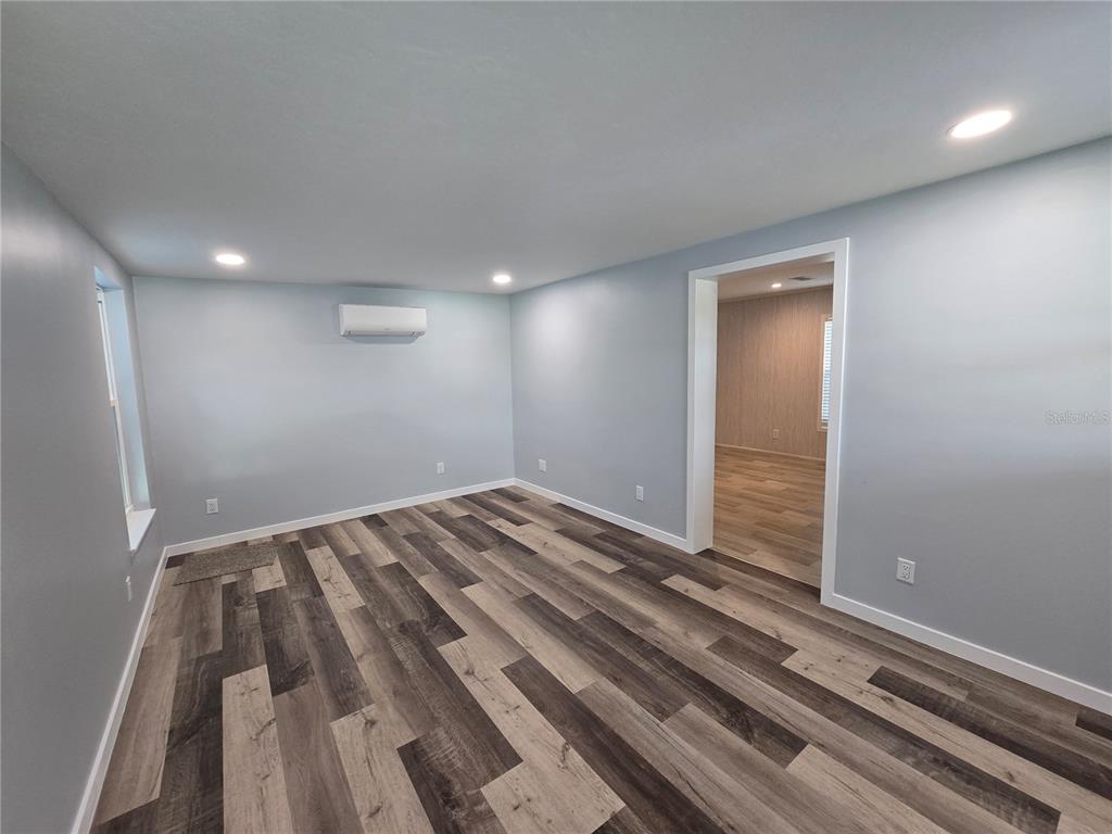 A room with light blue walls, wood-look flooring, recessed lighting, and a wall-mounted air conditioner — 1359 IBIS DRIVE, ENGLEWOOD, FL