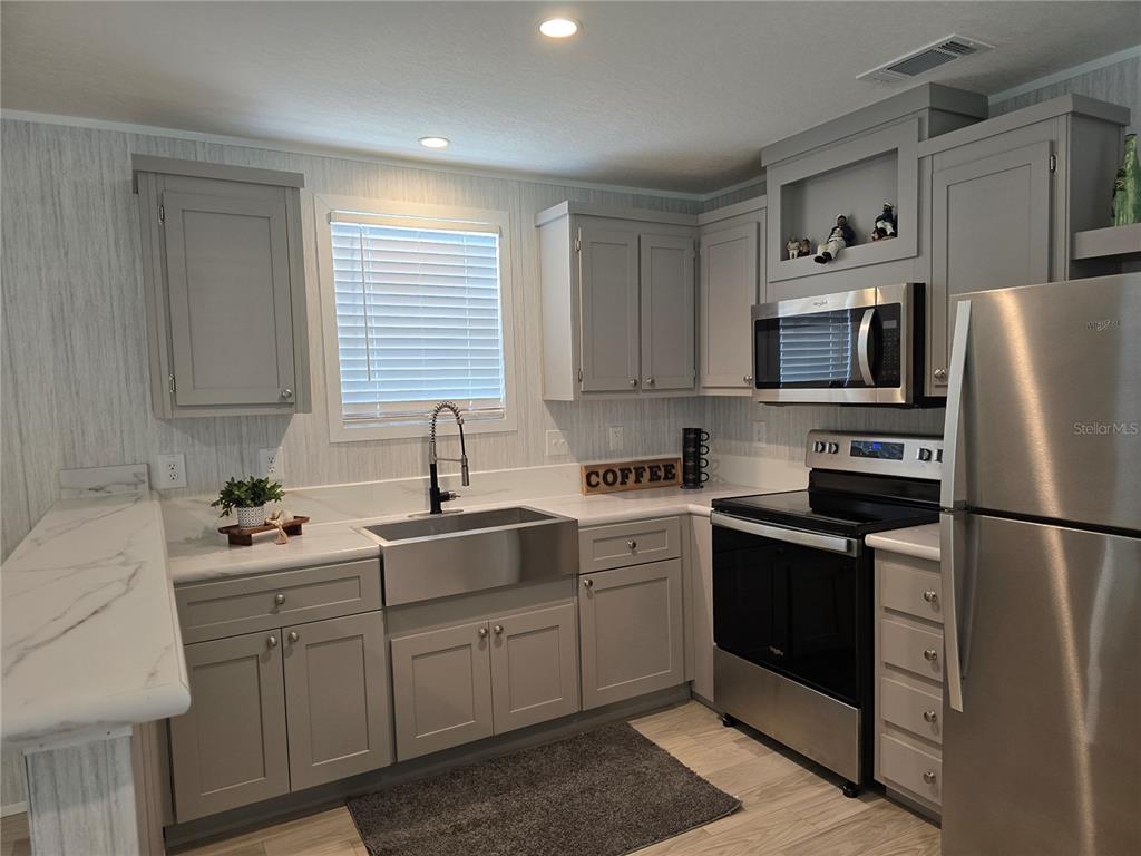 A kitchen features grey cabinets, stainless steel appliances, a farmhouse sink, and marble-look countertops — 1359 IBIS DRIVE, ENGLEWOOD, FL