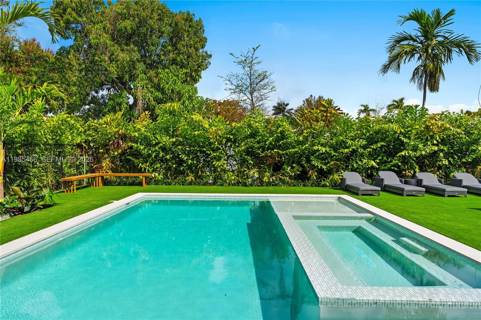 A rectangular swimming pool with an integrated spa sits on a lawn with lounge chairs — 245 NE 116th St, Miami FL 33161, MIAMI, FL