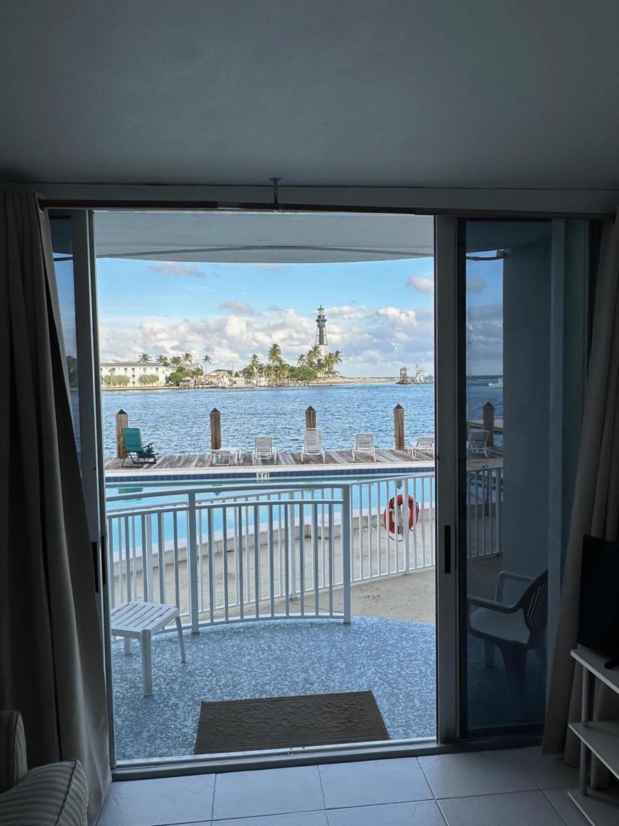 A view from a room through sliding glass doors looking out toward a lighthouse and water — 2508 Bay Drive, Pompano Beach FL 33062, POMPANO BEACH, FL