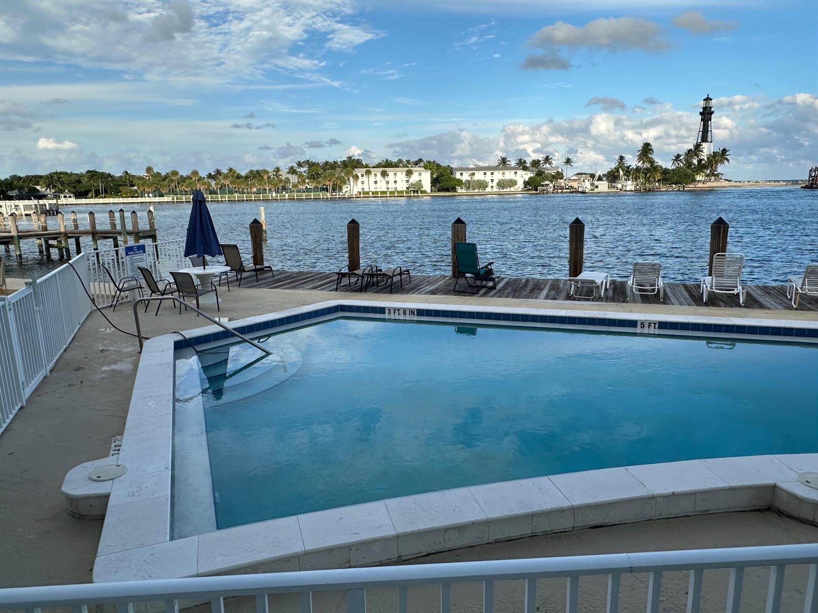 A swimming pool sits on a deck overlooking a waterway with a lighthouse in the distance — 2508 Bay Drive, Pompano Beach FL 33062, POMPANO BEACH, FL
