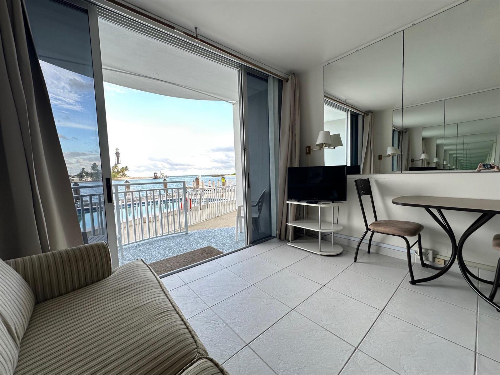 A living area with tile floors, a television, and a sliding door opening to a balcony — 2508 Bay Drive, Pompano Beach FL 33062, POMPANO BEACH, FL
