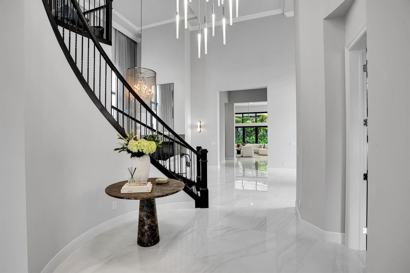 A grand foyer features a curved staircase, marble floors, and a modern tiered chandelier — 6903 NW 28th Avenue, Boca Raton FL 33496, BOCA RATON, FL