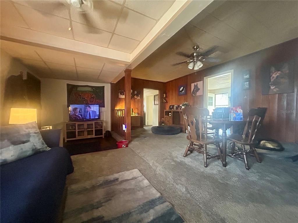 A living room and dining area feature wood-paneled walls, carpeted floors, and a ceiling fan — 2628 45TH AVENUE W, BRADENTON, FL