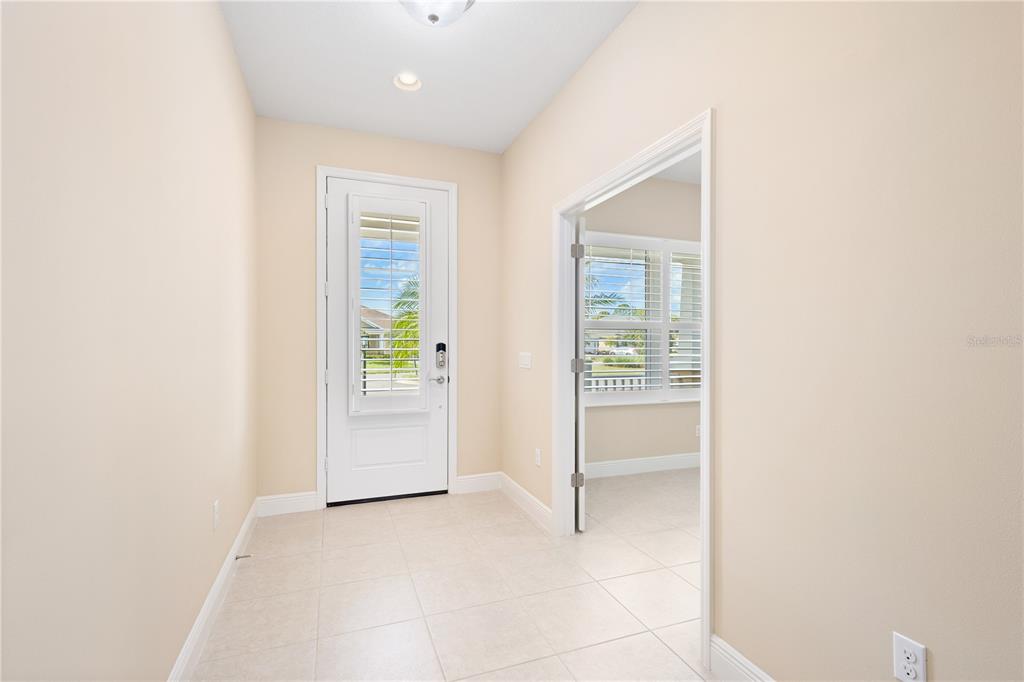 An entryway with light tile flooring, a white front door, and an open doorway — 3835 AUTUMN FERN TERRACE, SARASOTA, FL