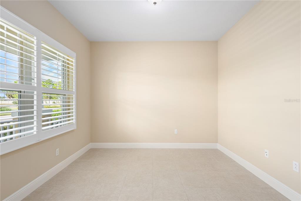 An empty room with beige walls, tile flooring, and white plantation shutters on the window — 3835 AUTUMN FERN TERRACE, SARASOTA, FL