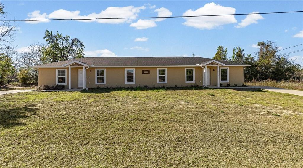 A single-story duplex with a tan exterior, two front entrances, and a large grassy yard — 5364 NW 2ND PLACE, OCALA, FL