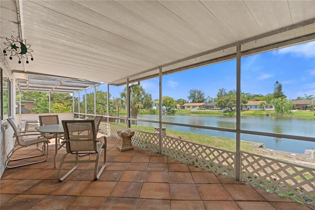 A screened-in patio with tile flooring overlooks a lake and neighboring houses — 3531 LANDALE DRIVE, HOLIDAY, FL