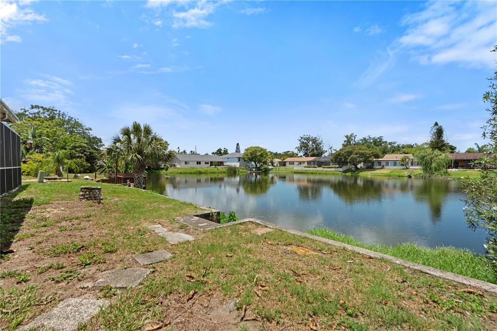 A grassy backyard overlooks a calm pond with residential houses visible on the opposite shore — 3531 LANDALE DRIVE, HOLIDAY, FL