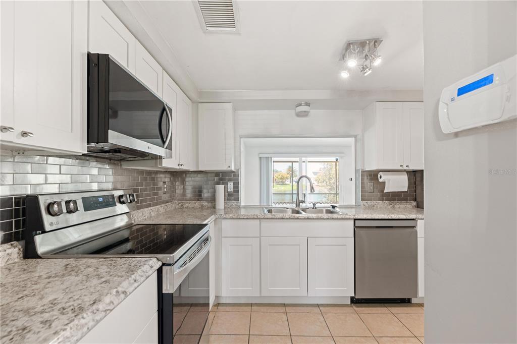 A kitchen features white cabinets, granite countertops, stainless steel appliances, and a gray subway tile backsplash — 3531 LANDALE DRIVE, HOLIDAY, FL