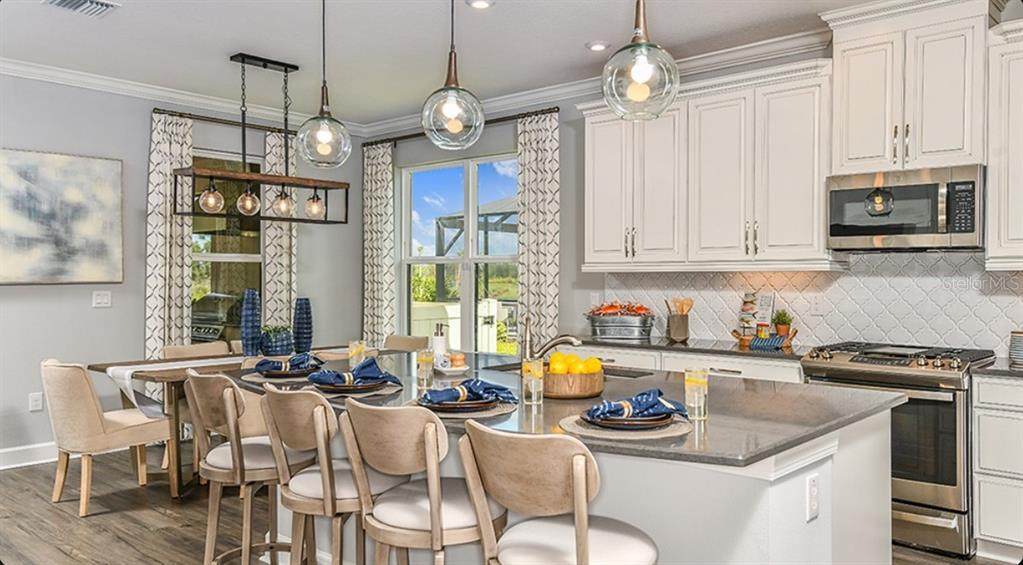 A kitchen features a large island with bar seating, white cabinets, and pendant lighting — 3946 MASANIELLO WAY, WESLEY CHAPEL, FL