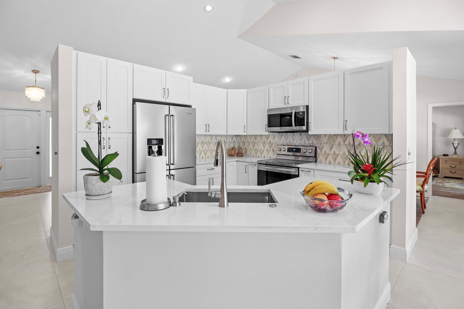 A modern kitchen features white cabinets, stainless steel appliances, and a white quartz island countertop — 9260 Laurel Green Drive, Boynton Beach FL 33437, BOYNTON BEACH, FL