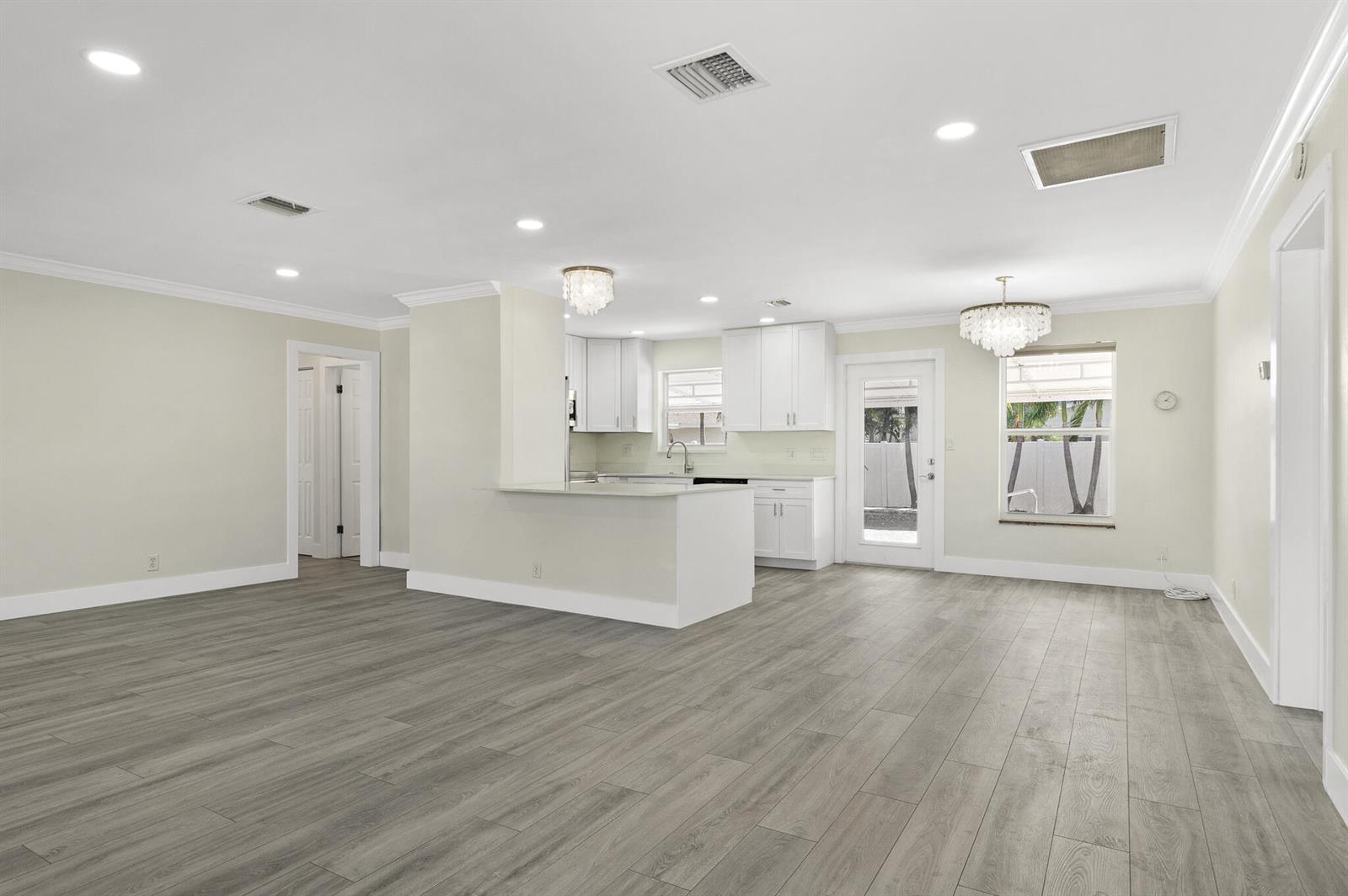 An open-concept kitchen and living area features white cabinetry, light walls, and gray wood flooring — 912 SE 8th Court, Deerfield Beach FL 33441, DEERFIELD BEACH, FL