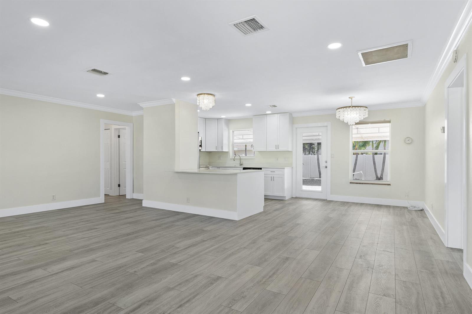 An open-concept kitchen and dining area features white cabinetry, light wood-look flooring, and chandeliers — 912 SE 8th Court, Deerfield Beach FL 33441, DEERFIELD BEACH, FL