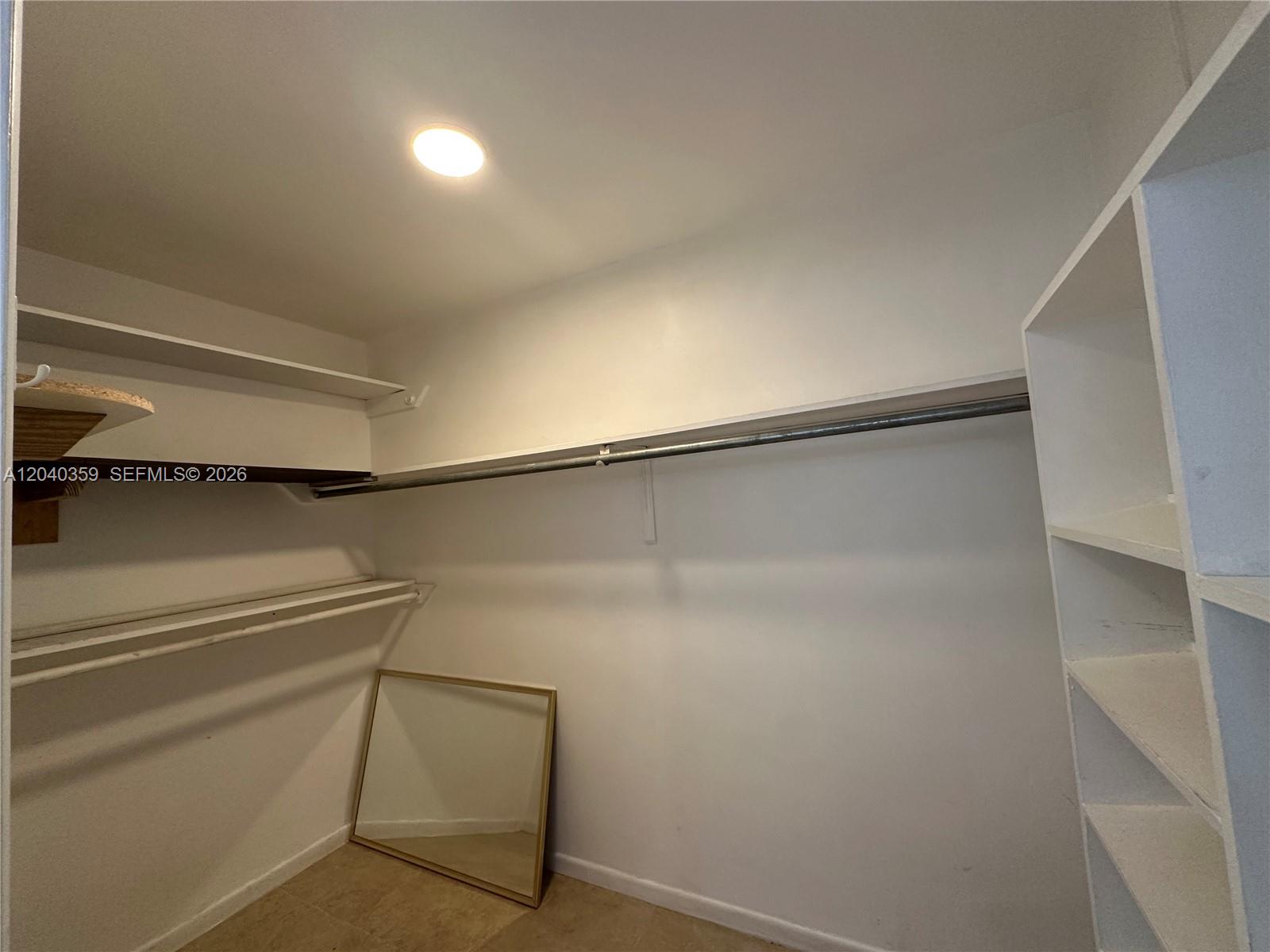 A walk-in closet features white shelving, a metal hanging rod, and a floor-standing mirror — 819 NE 8th St # 2, Hallandale Beach FL 33009, HALLANDALE BEACH, FL