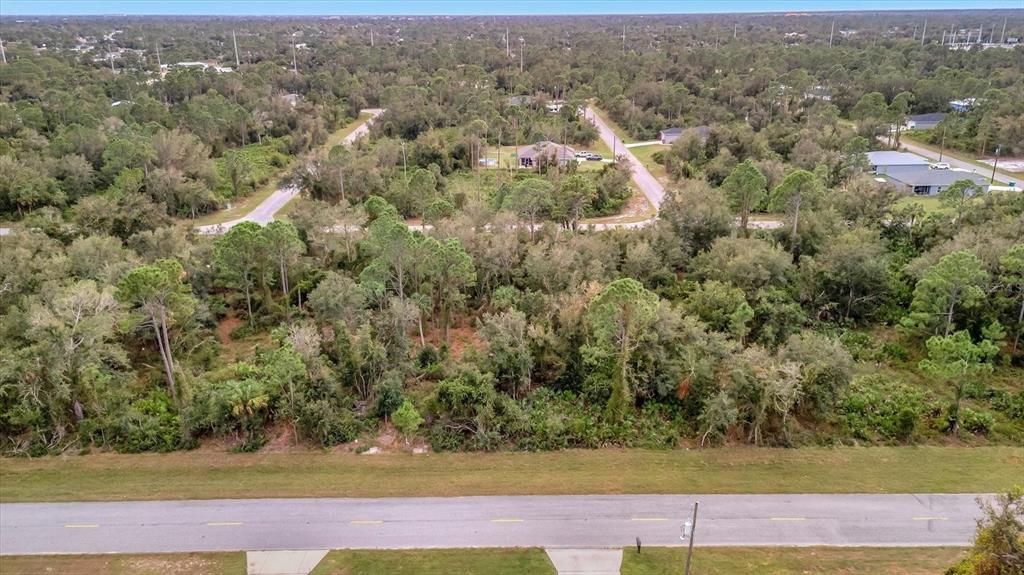 An aerial view shows a wooded, undeveloped lot situated between a paved road and houses — 21035 HILLSBOROUGH BOULEVARD, PORT CHARLOTTE, FL