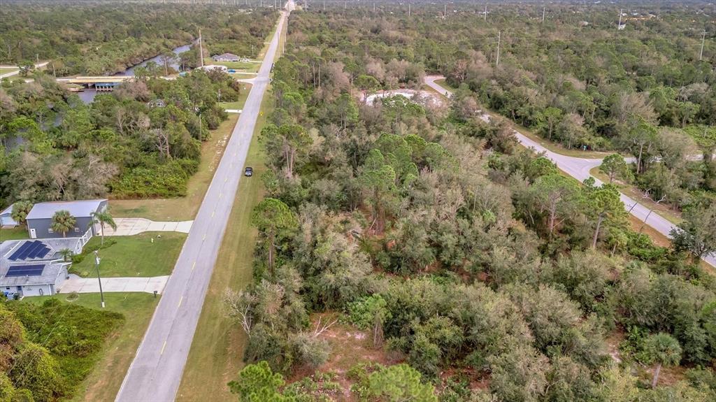 An aerial view shows a paved road running through a wooded area with nearby houses — 21035 HILLSBOROUGH BOULEVARD, PORT CHARLOTTE, FL