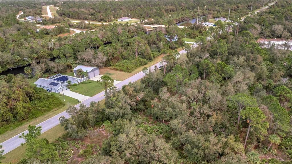 An aerial view shows a house with a detached garage beside a wooded road — 21035 HILLSBOROUGH BOULEVARD, PORT CHARLOTTE, FL