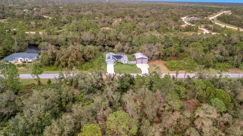 An aerial view shows a house with solar panels and a detached garage near woods — 21035 HILLSBOROUGH BOULEVARD, PORT CHARLOTTE, FL