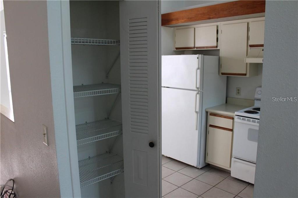 A kitchen features white appliances, light-colored cabinets, tiled floors, and an open pantry with shelving — 2906 S SEMORAN BOULEVARD UNIT 2, ORLANDO, FL