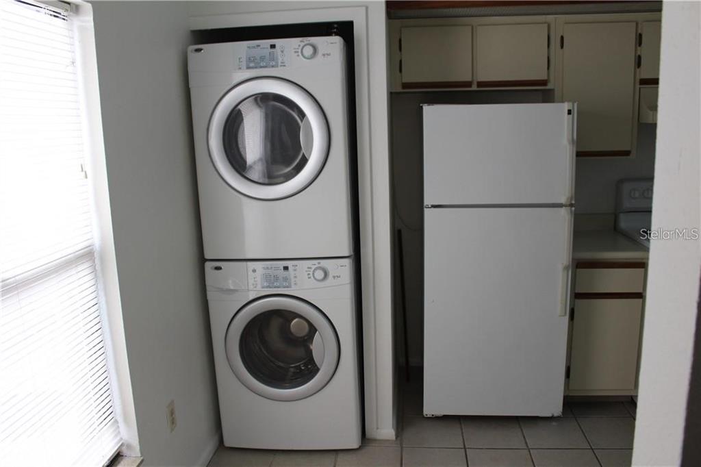 A stacked washer and dryer unit stands next to a white refrigerator in a kitchen — 2906 S SEMORAN BOULEVARD UNIT 2, ORLANDO, FL