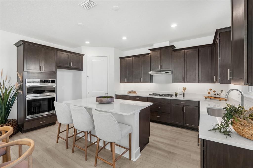 A modern kitchen features dark wood cabinets, white countertops, a central island, and stainless appliances — 716 MYSTIC GARDENS DRIVE, APOPKA, FL