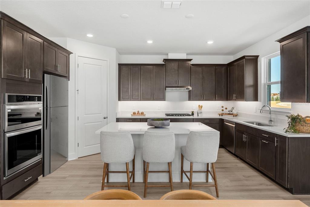 A modern kitchen features dark wood cabinetry, a white island with three stools, and stainless appliances — 716 MYSTIC GARDENS DRIVE, APOPKA, FL