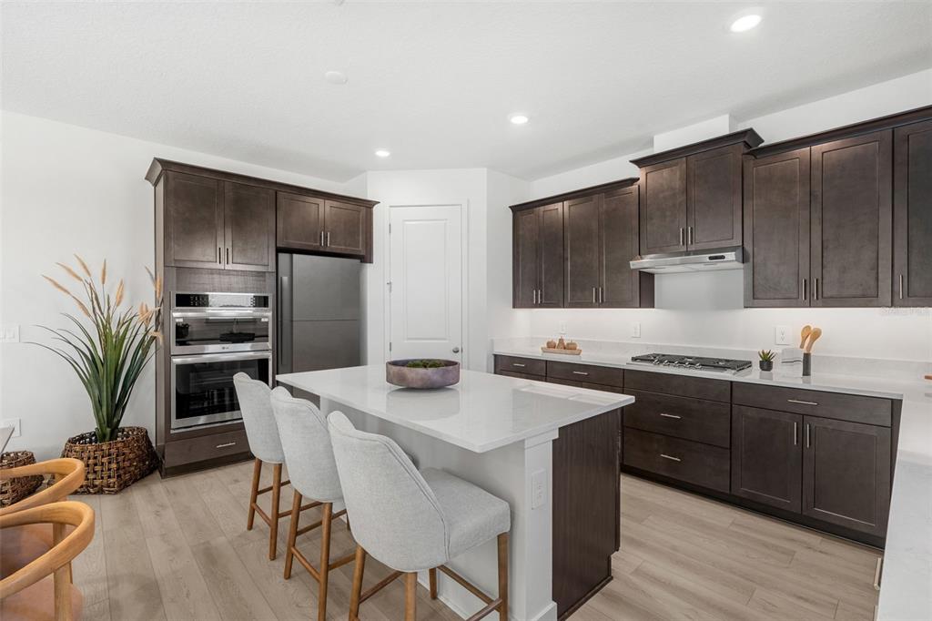A modern kitchen features dark wood cabinets, a white quartz island, and light wood flooring — 716 MYSTIC GARDENS DRIVE, APOPKA, FL