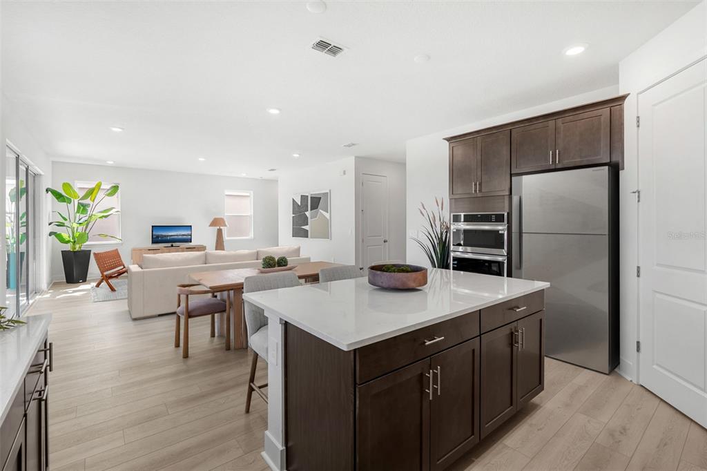 A modern kitchen with a white island and dark cabinets opens into a living area — 716 MYSTIC GARDENS DRIVE, APOPKA, FL