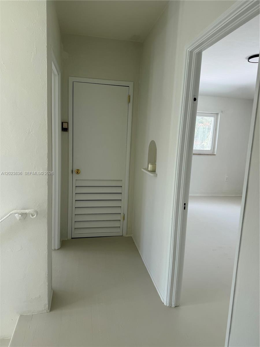 A hallway with light-colored walls and flooring leads to a closed louvered door — 6312 Alton Rd, Miami Beach FL 33141, MIAMI BEACH, FL