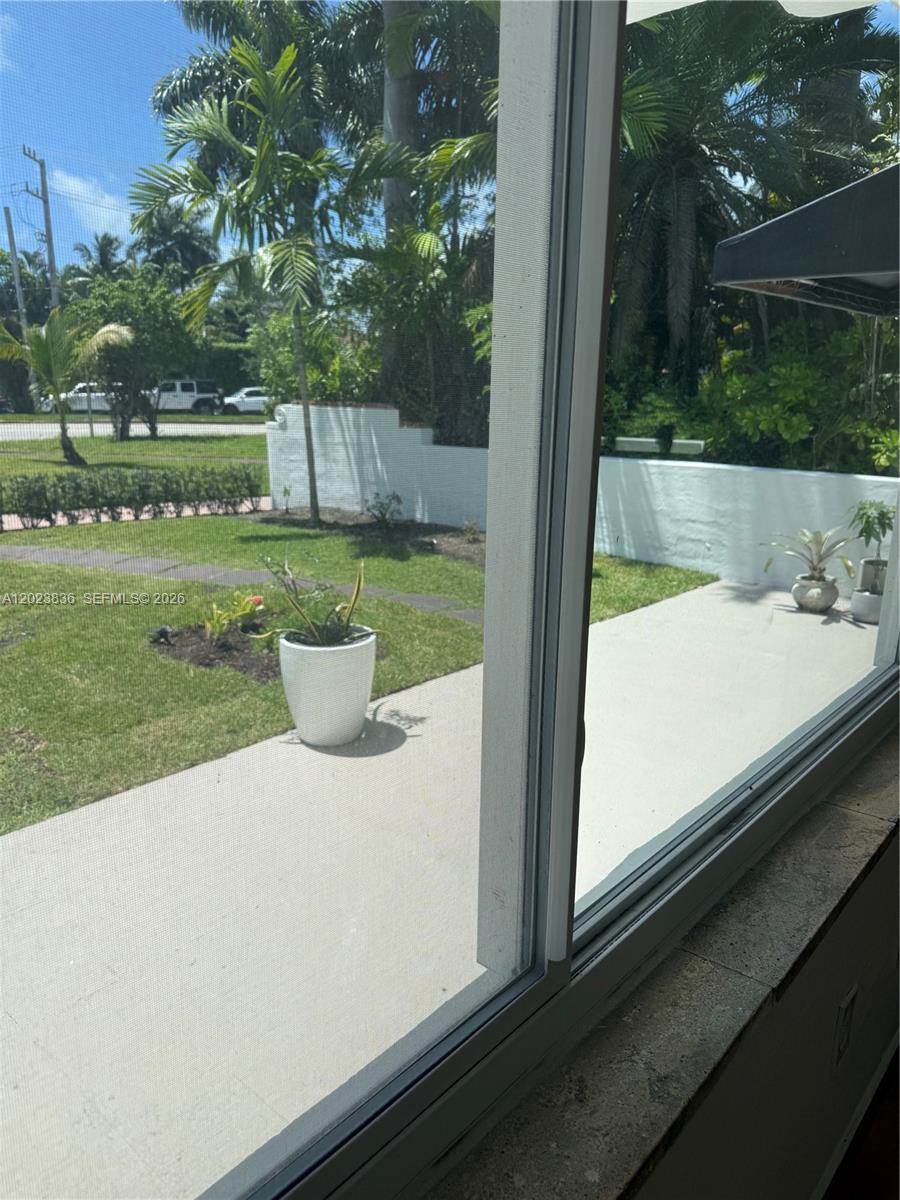 A view through a window shows a concrete patio, a lawn, and a white wall — 6312 Alton Rd, Miami Beach FL 33141, MIAMI BEACH, FL
