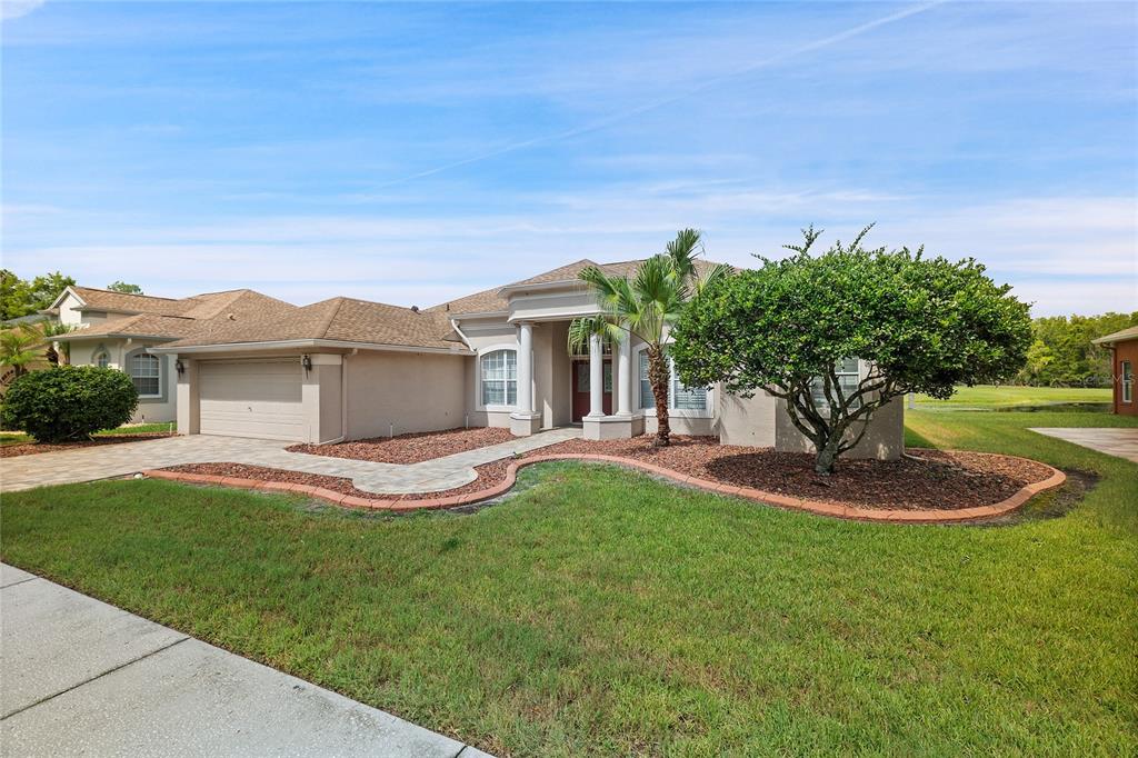 A single-story house with a tan stucco exterior, a two-car garage, and a landscaped yard — 7154 MELOGOLD CIRCLE, LAND O LAKES, FL