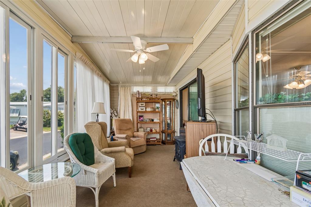 A sunroom features a ceiling fan, carpeted flooring, wicker chairs, and large windows — 12501 ULMERTON ROAD UNIT 175, LARGO, FL