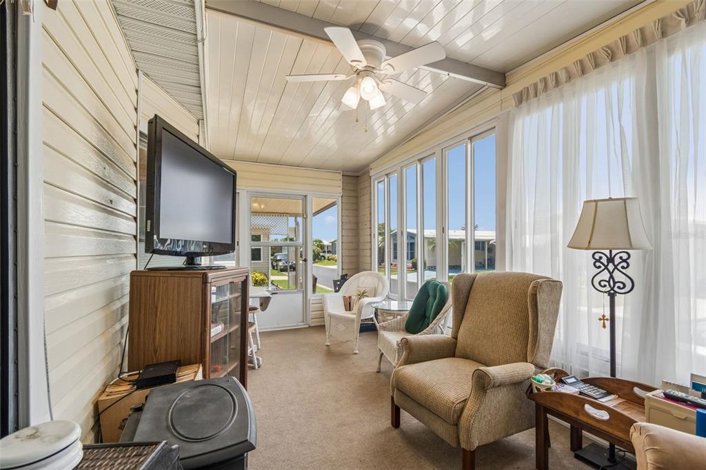 A sunroom features a ceiling fan, carpeted flooring, a television, and large windows with curtains — 12501 ULMERTON ROAD UNIT 175, LARGO, FL