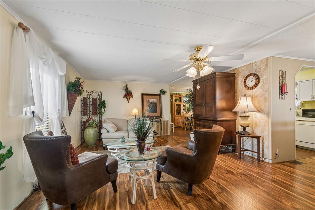 A living room features wood-look flooring, two brown armchairs, a sofa, and a ceiling fan — 12501 ULMERTON ROAD UNIT 175, LARGO, FL