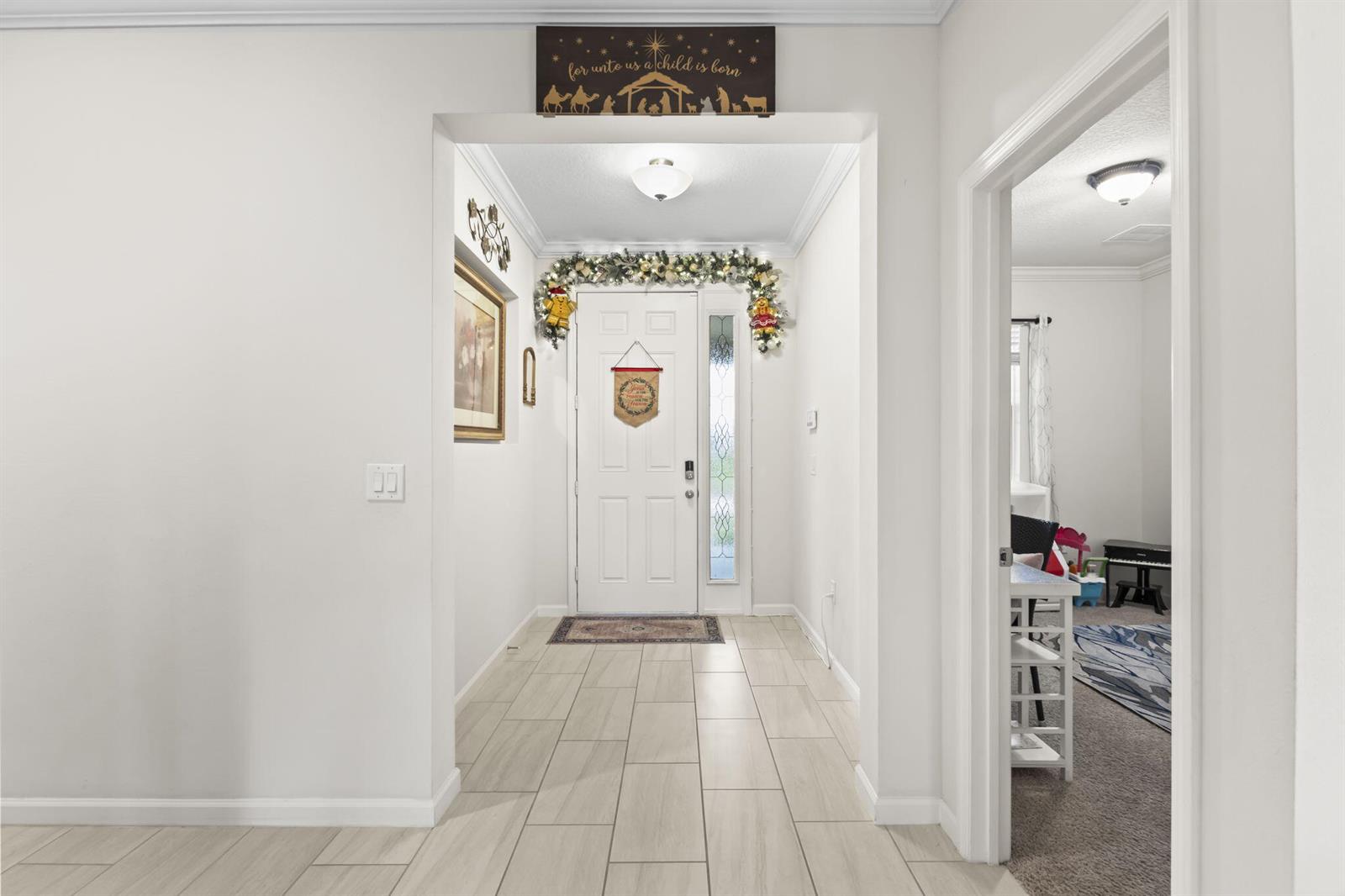 A white front door with holiday decor sits at the end of a tiled entryway — 1465 Bruntsfield Terrace, Vero Beach FL 32966, VERO BEACH, FL