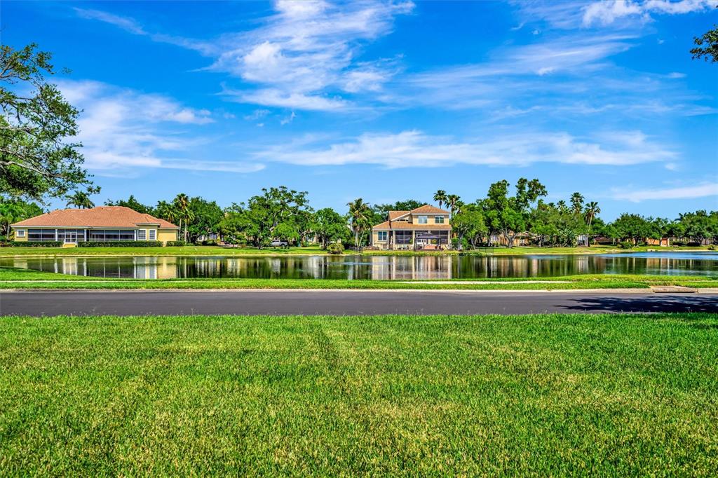 A grassy lawn overlooks a calm lake with two houses and trees in the background — 1846 AMBERWYND CIRCLE W, PALMETTO, FL